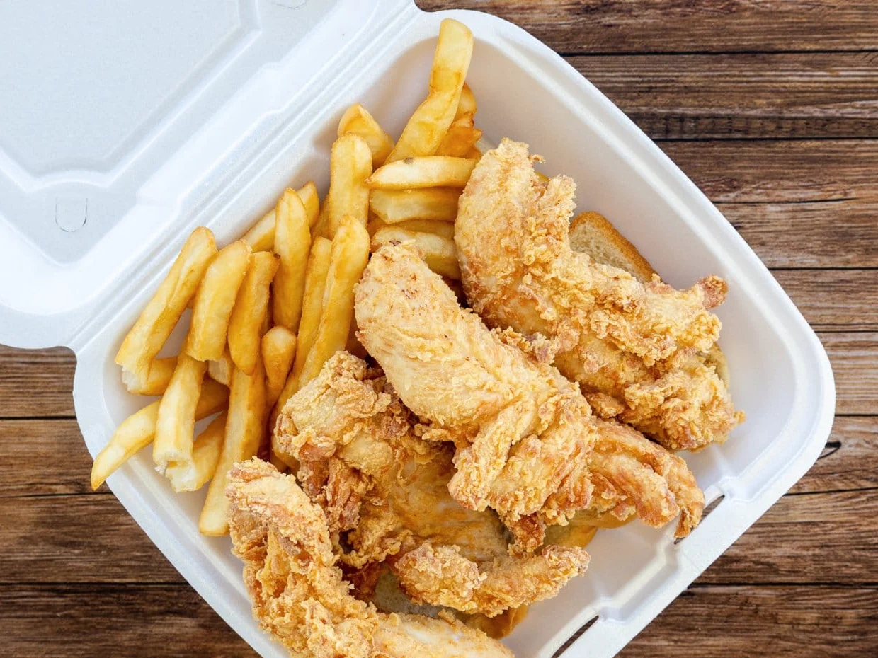 Breaded chicken tenders with fries in a takeout tray